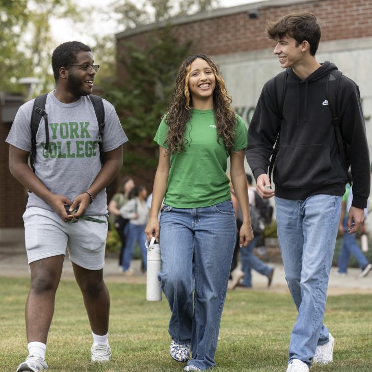 Three students walking together in front of a York College sign