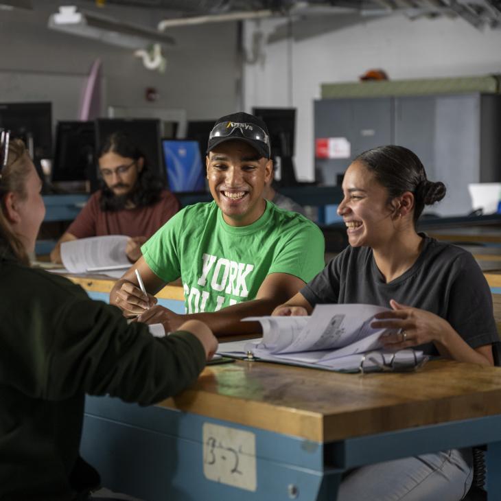 Students sit at a work table in a computer lab at YCP reviewing papers. Some collaborate and some work independently.