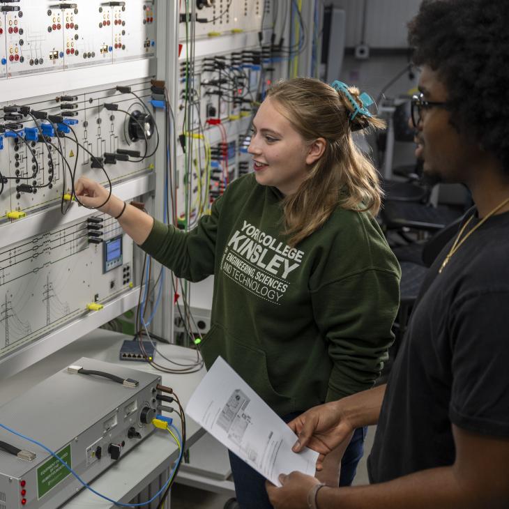 Two students in an undergraduate engineering program work on electrical control panels and wiring in a YCP lab.