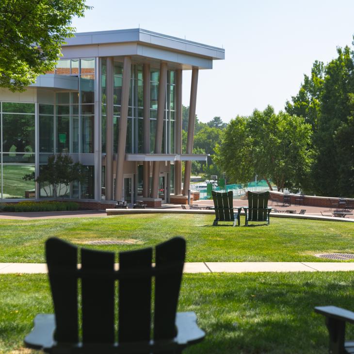 Adirondack chairs on a green lawn with a building with large glass windows in the background.
