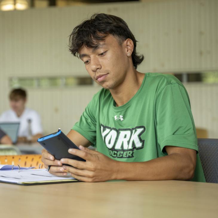A student wearing a green York Soccer shirt studying at a table.
