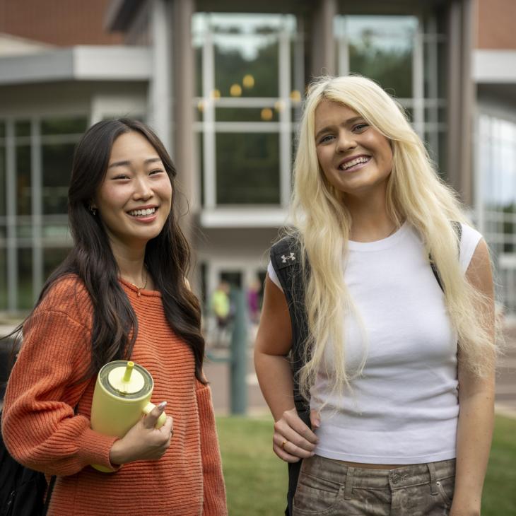 Two YCP students standing outside in front of a building with large glass windows.