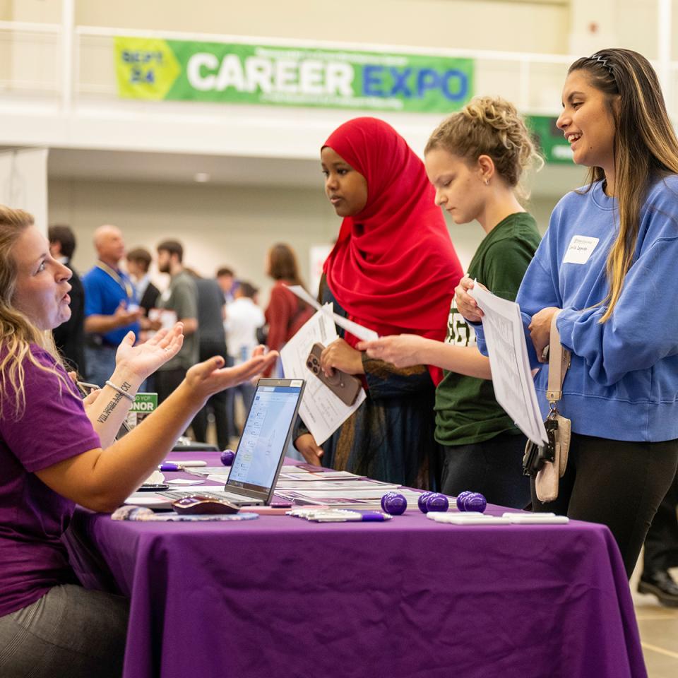 Three students speak to a businesswoman at the Career Expo