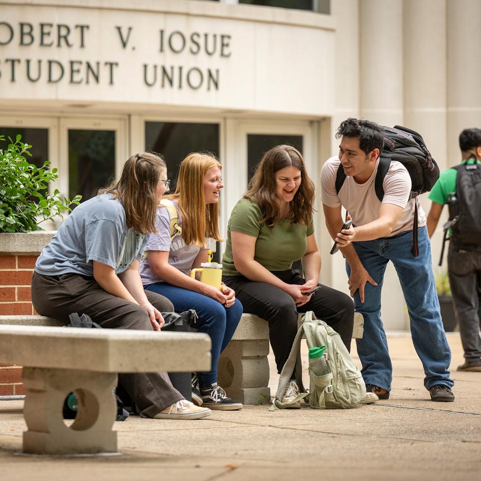 A group of student look at a cell phone in front of the student union