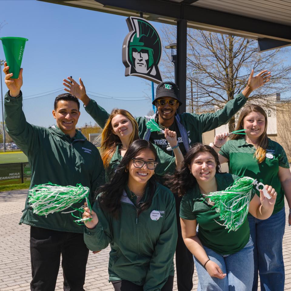 Six students pose together in front of the Spartan Log sign outside.