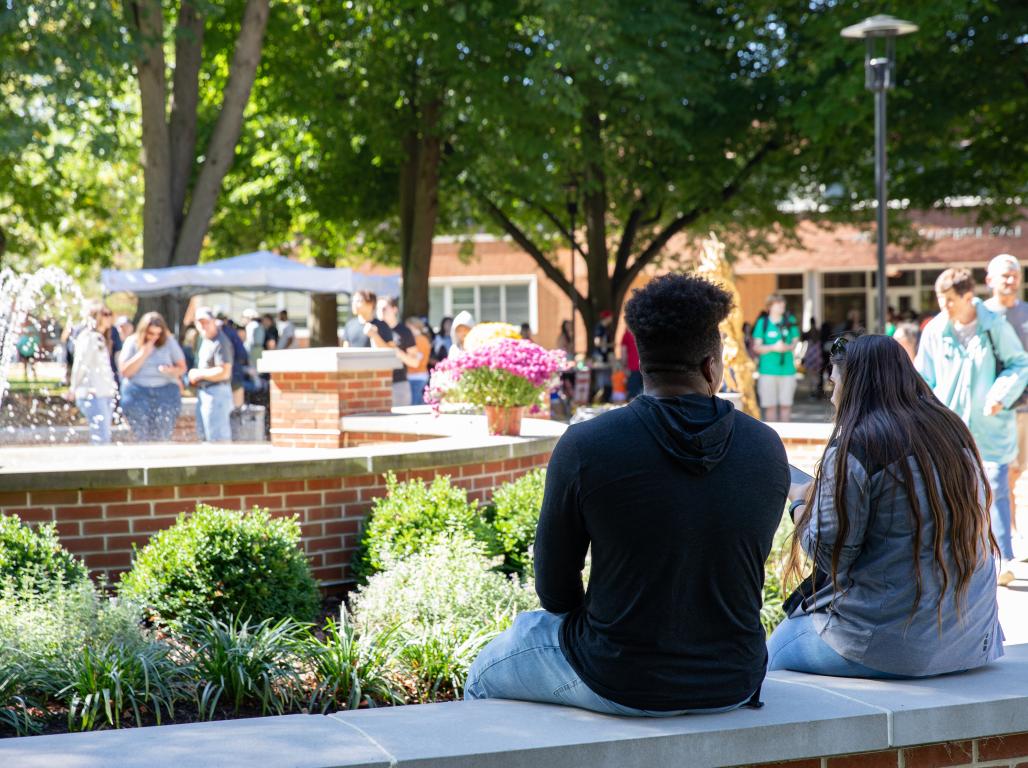 People relaxing and walking around an outdoor fountain on a sunny day.